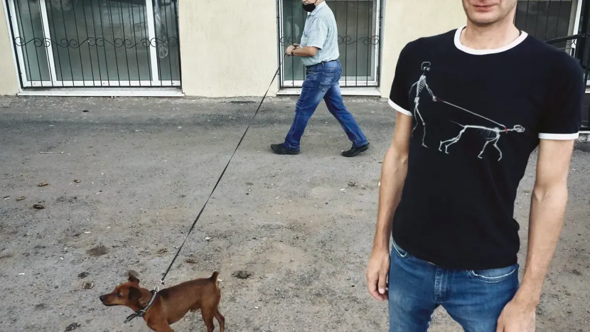 A dog walker holding a retractable leash handle while a dog explores ahead on a sidewalk
