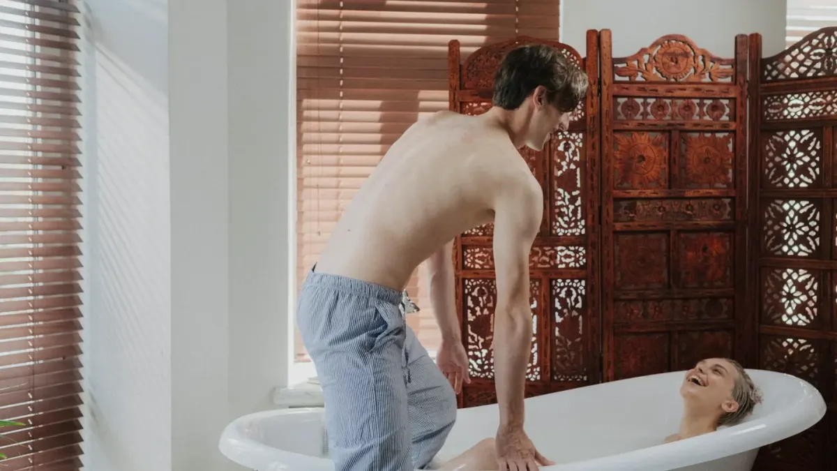 A large dog standing calmly in a tub while an owner rinses its coat