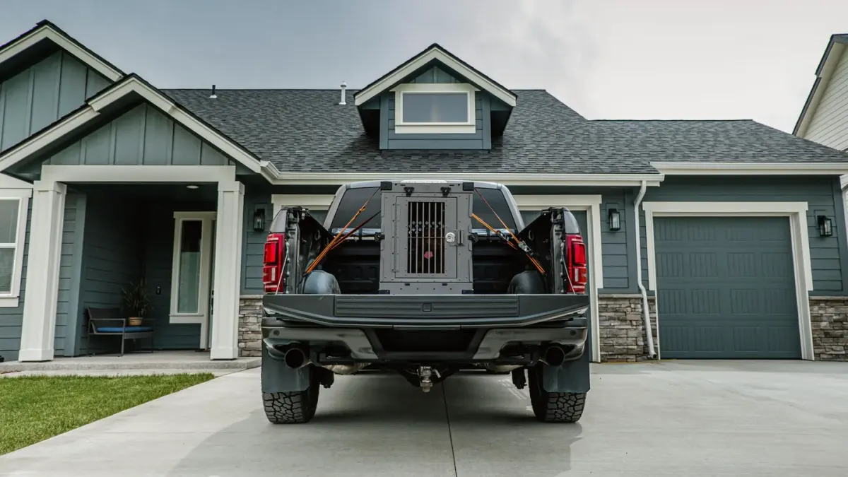 A medium-sized dog resting inside a secured travel crate in the back of an SUV