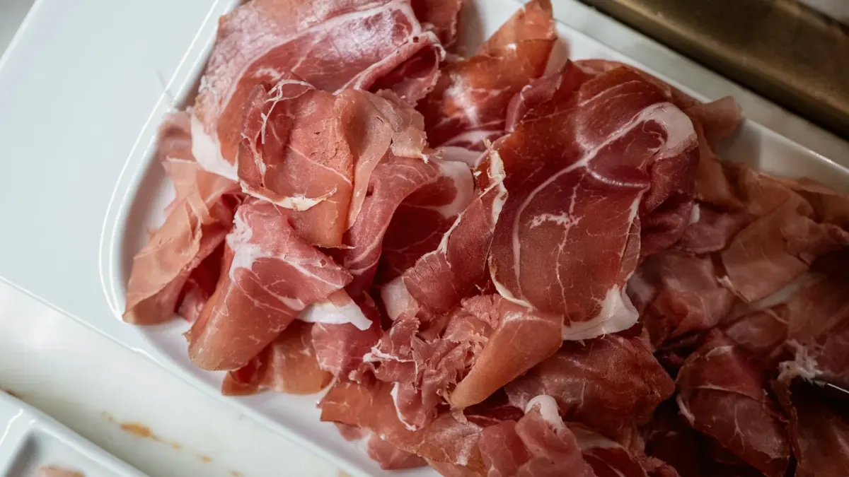 A plate of sliced ham on a kitchen counter with a dog watching from a few feet away