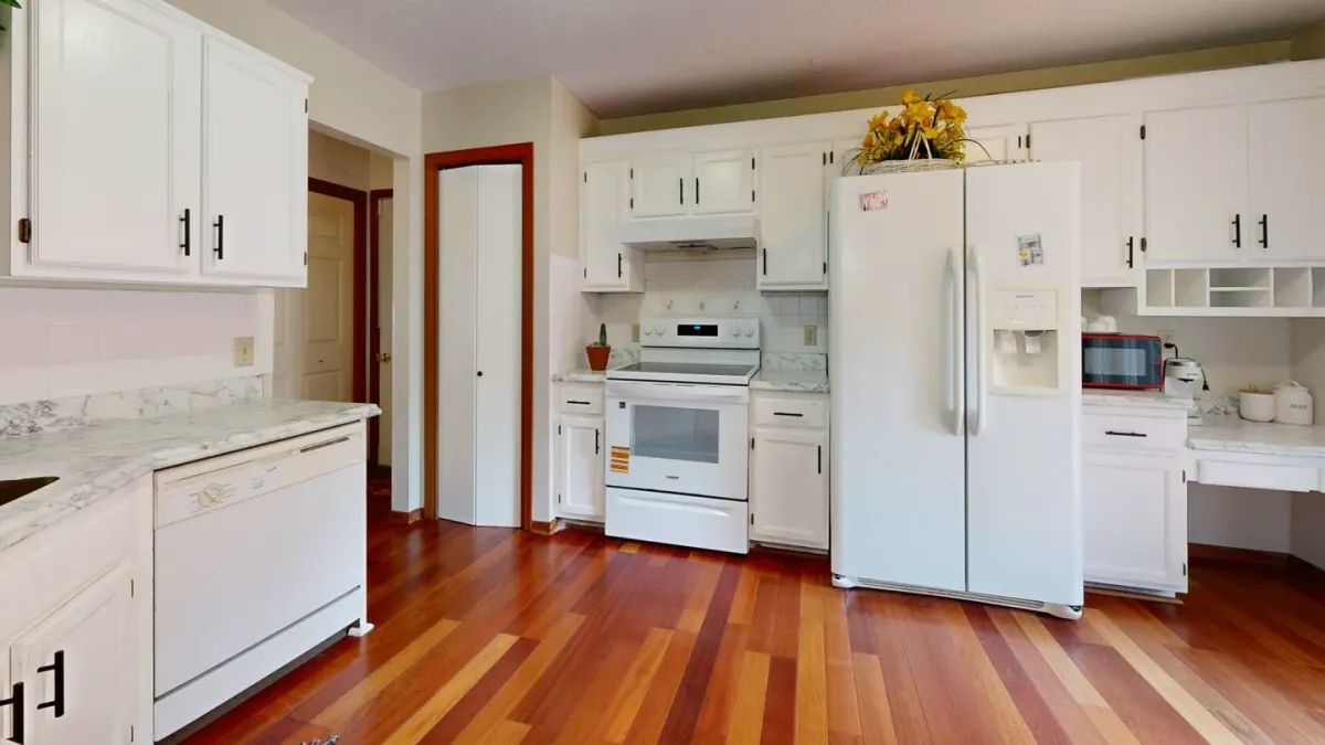 A puppy sitting on a kitchen floor looking up near open lower cabinets
