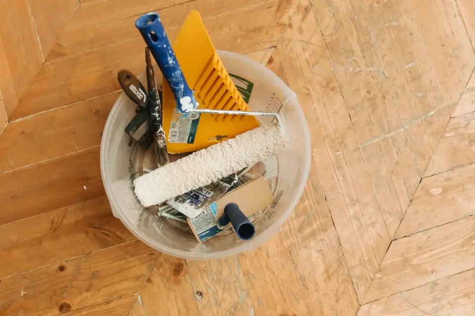 A slicker brush resting on a wood floor near a dog's paw