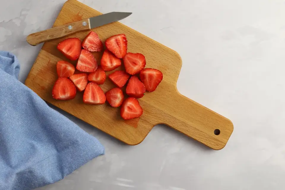 A small dog sniffing sliced strawberries on a wooden cutting board