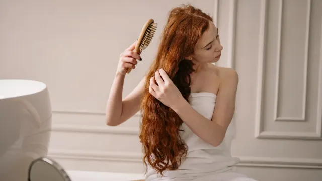 An owner kneeling beside a dog on a towel, brush in hand, during a calm at-home grooming session