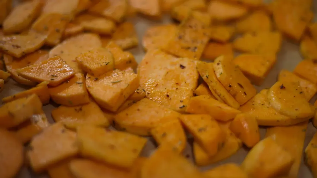 Cubed cooked sweet potato on a cutting board next to a dog looking up