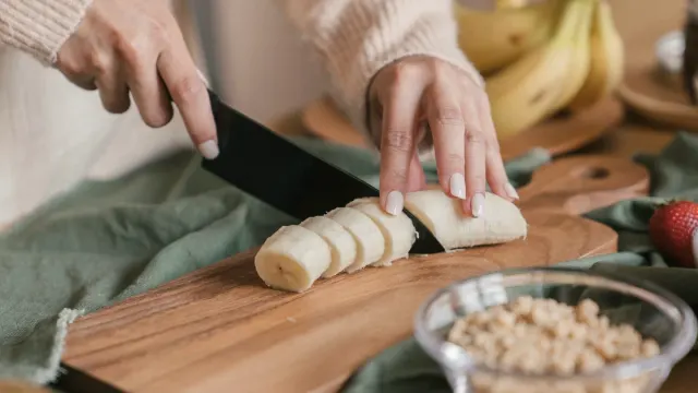 Fresh banana slices arranged on a wooden cutting board beside an empty dog bowl