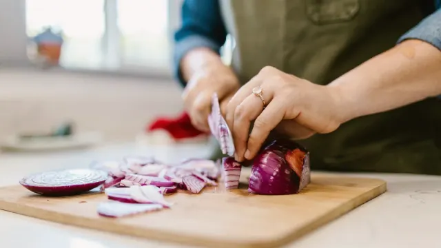 Sliced onions on a cutting board while a dog waits nearby in the kitchen