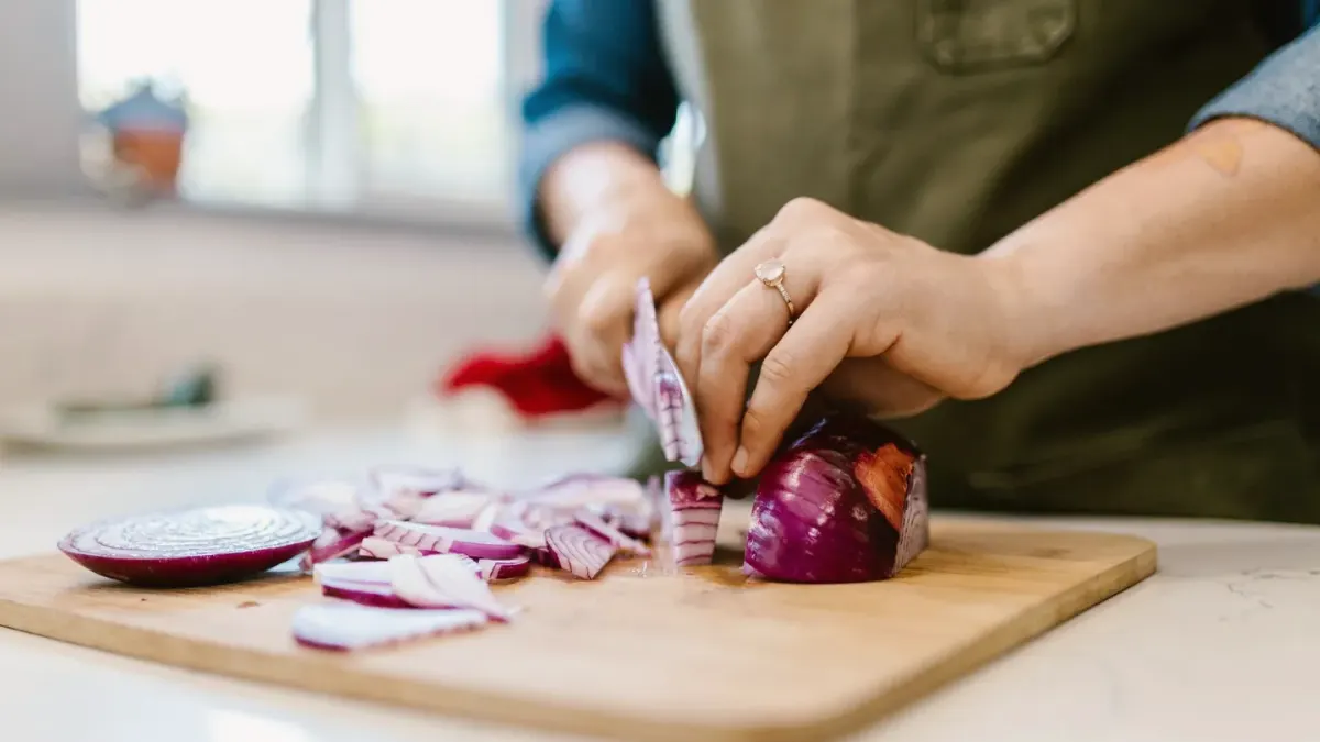 Sliced onions on a cutting board while a dog waits nearby in the kitchen