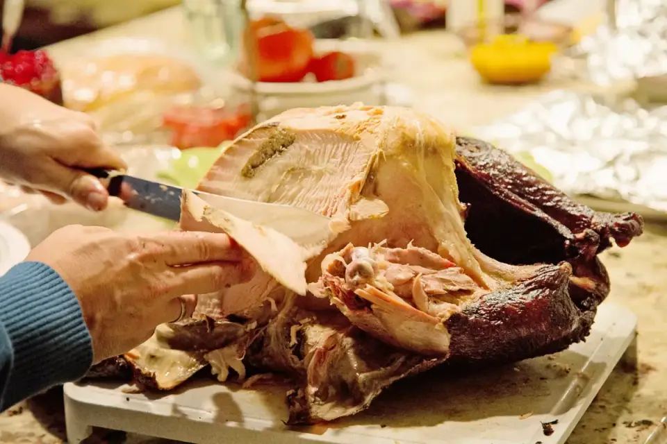 Sliced roast turkey breast on a wooden cutting board with a dog watching a few feet away